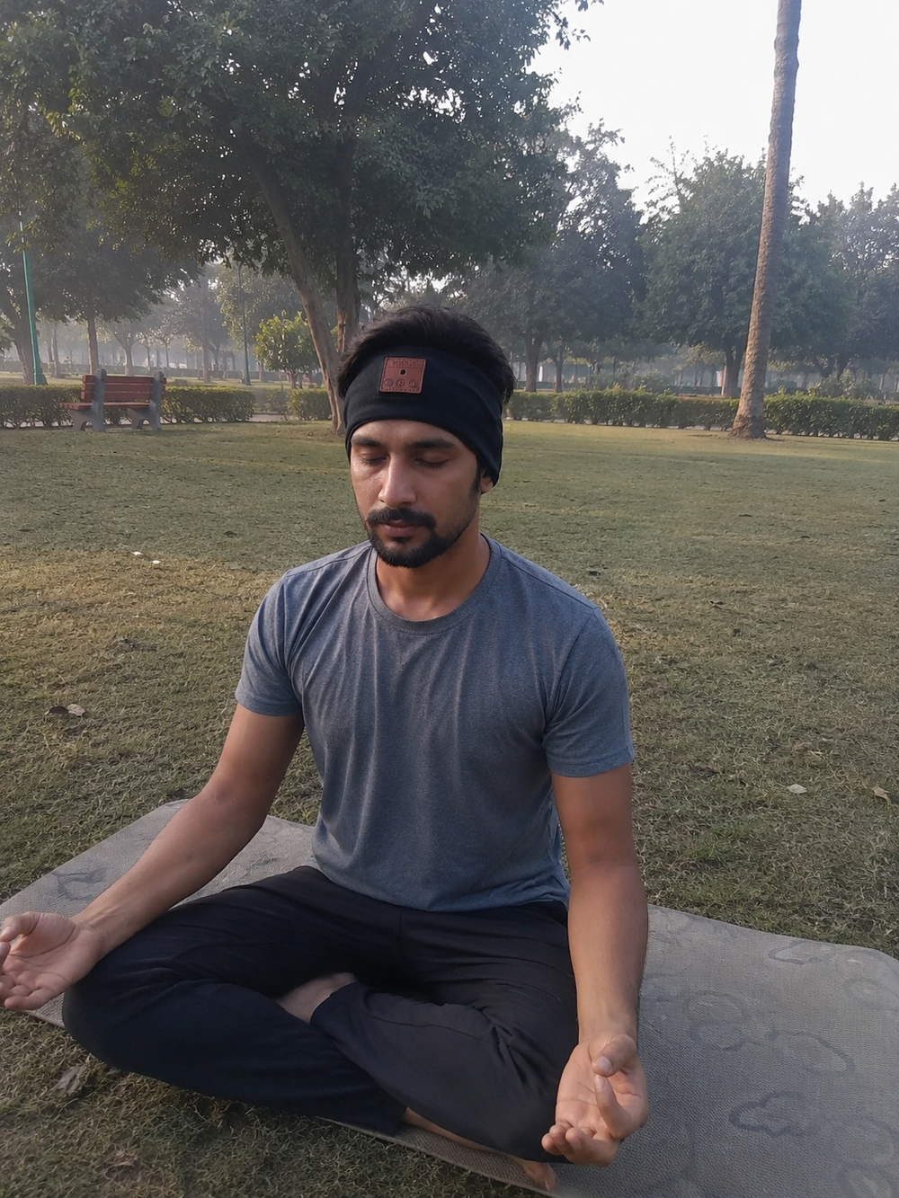 Man meditating on a stone bench in a park with trees and grass in the background with beatband.